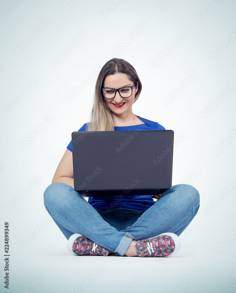 Naklejka premium Happy young woman with smile working or typing on laptop while sitting in lotus pose on the floor over light background