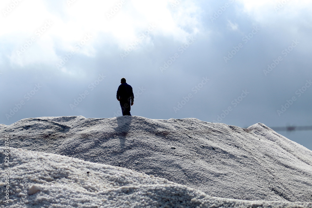 Man silhouette standing on salt mountain in industrial salt marsh 