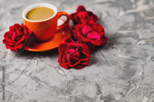 Full cup of coffee with milk beside red roses on old gray concrete surface. Love concept