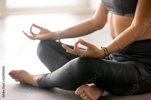 Young sporty yogi woman practicing yoga, doing Easy Seat exercise, Sukhasana pose, working out wearing sportswear grey pants, top, indoor body and legs close up at yoga studio. Hobby wellbeing concept