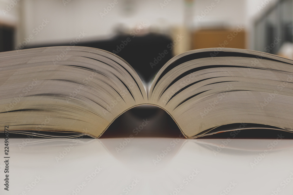 Naklejka premium Open book on table and blurred bookshelf. Education background.
