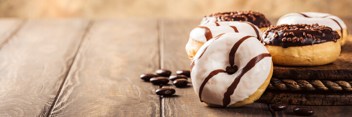 Glazed mini donuts with coffee candies on wooden background. Party food concept with copy space. Banner.