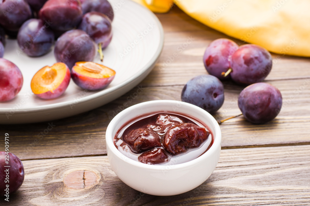 Appetizing jam from blue plum and a bunch of ripe berries on a plate on a wooden table Appetizing jam from blue plum and a bunch of ripe berries on a plate on a wooden table