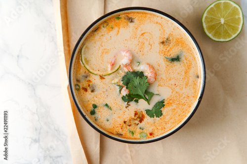 Tom yum soup with shrimps, traditional thai spicy dish served with cilantro and lime slices on marble table. Top view with copy space