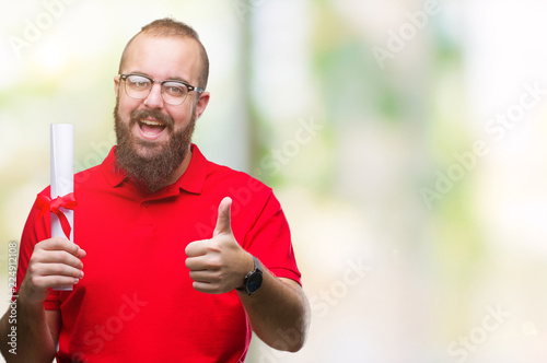 Young hipster man wearing glasses and holding degree over isolated background happy with big smile doing ok sign, thumb up with fingers, excellent sign