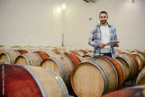 handsome man winemaker in a maturing wine cellar winery during harvest season with oak barrels