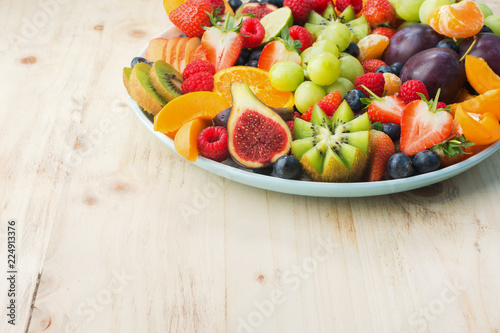 Healthy fruit and berries platter  strawberries raspberries oranges plums apples kiwis grapes blueberries on the light wooden pine table  close up  copy space for text  square  selective focus