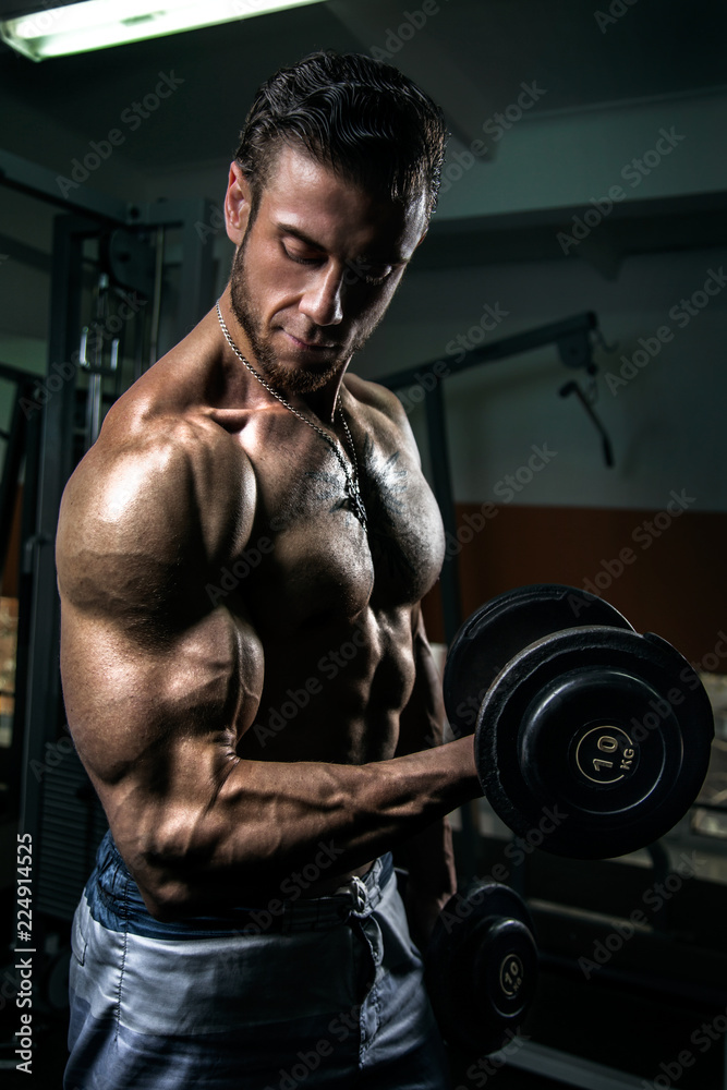 White Muscular man training his biceps in the gym by dumbbells