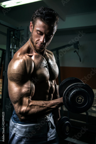 White Muscular man training his biceps in the gym by dumbbells
