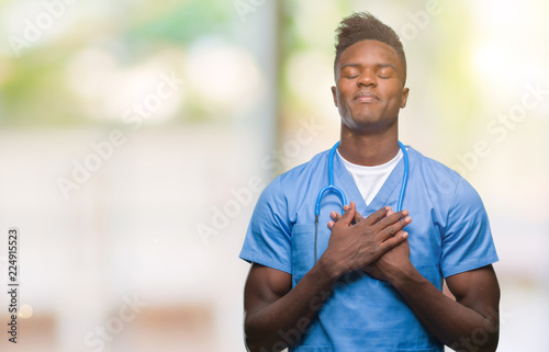 Young african american doctor man over isolated background wearing surgeon uniform smiling with hands on chest with closed eyes and grateful gesture on face. Health concept.
