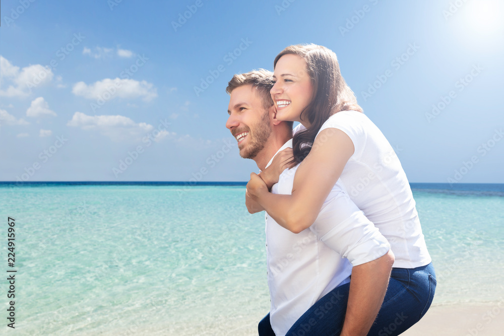 Happy Man Giving Piggyback To His Wife At Beach Happy Man Giving Piggyback To His Wife At Beach