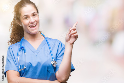 Young brunette doctor girl wearing nurse or surgeon uniform over isolated background with a big smile on face, pointing with hand and finger to the side looking at the camera.
