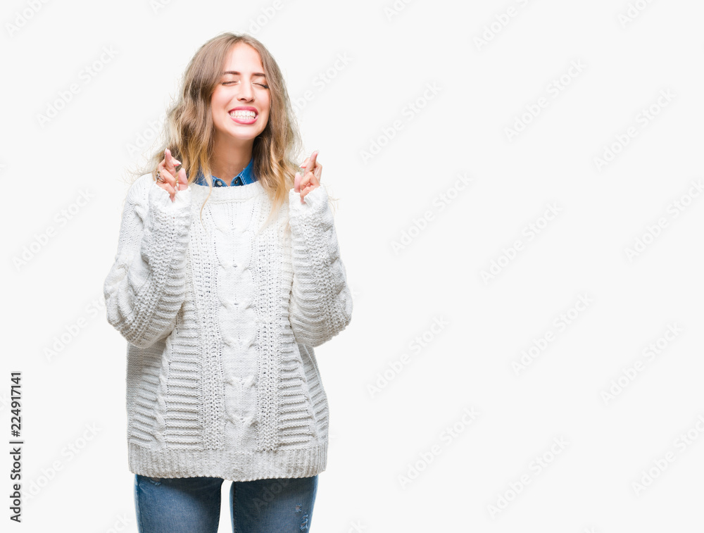 Beautiful young blonde woman wearing winter sweater over isolated background smiling crossing fingers with hope and eyes closed. Luck and superstitious concept. Beautiful young blonde woman wearing winter sweater over isolated background smiling crossing fingers with hope and eyes closed. Luck and superstitious concept.
