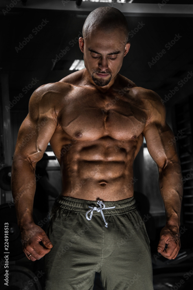 White Muscular man fitness model is posing in the gym and looking down