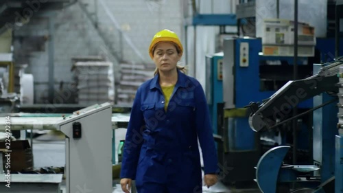 Wallpaper Mural Middle-aged woman in blue workwear and yellow safety helmet walking through industrial facility Torontodigital.ca