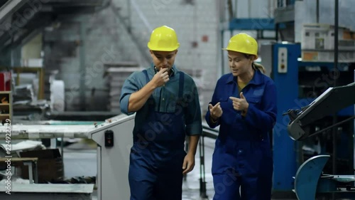 Front view of interested middle aged woman in hardhat explaining work process to male colleague while walking through factory