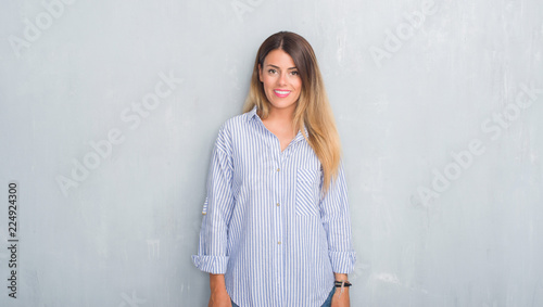 Young adult woman over grey grunge wall wearing fashion business outfit with a happy and cool smile on face. Lucky person.