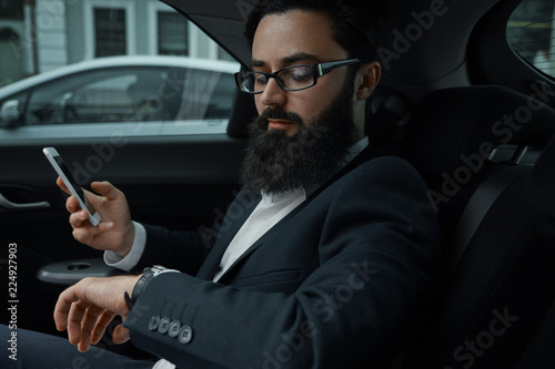 A businessman while traveling by car in the back seat using a sm