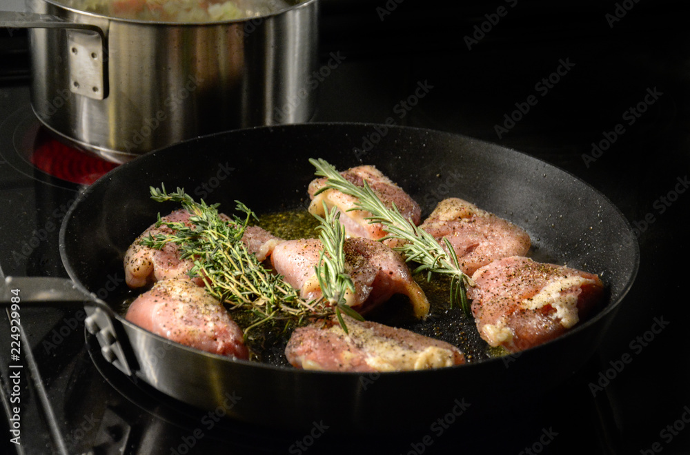 A large fryer is cooking a tasty chicken with butter and rosemary spice in the foreground and a pan with rice in the background over a stove A large fryer is cooking a tasty chicken with butter and rosemary spice in the foreground and a pan with rice in the background over a stove