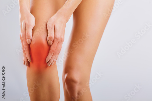 Pain, injury to the knee. A woman holds her knee with her hand.