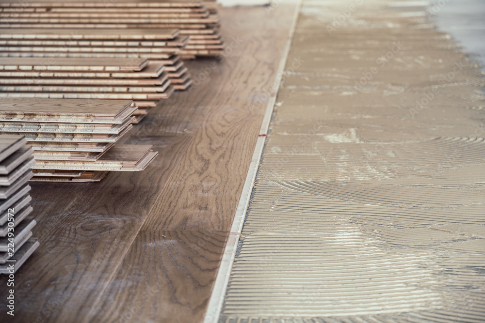 Laminated wooden boards installed on concrete floor with applied adhesive