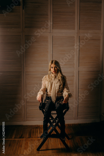 Beautiful luxurious blonde woman sitting on chair on a dark textural background. Studio shot.