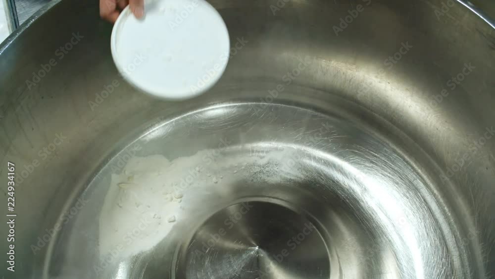 Hands of unrecognizable cook adding flour into empty industrial dough kneading machine at factory Hands of unrecognizable cook adding flour into empty industrial dough kneading machine at factory