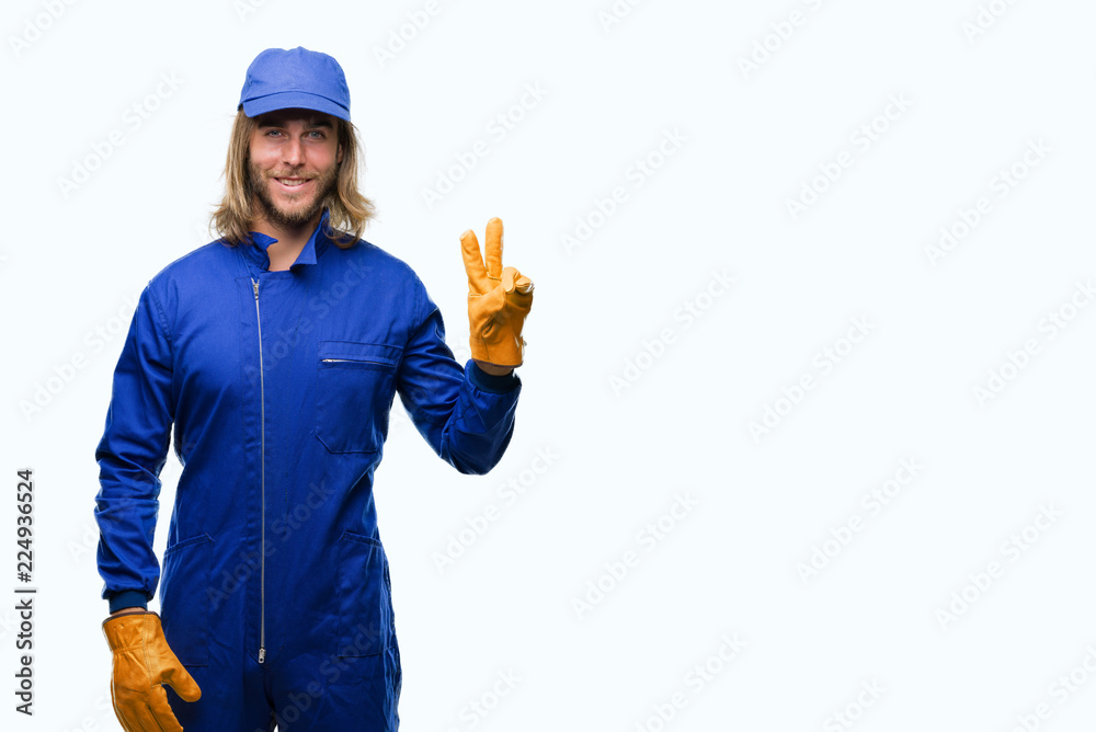 Young handsome mechanic man with long hair over isolated background smiling with happy face winking at the camera doing victory sign. Number two.