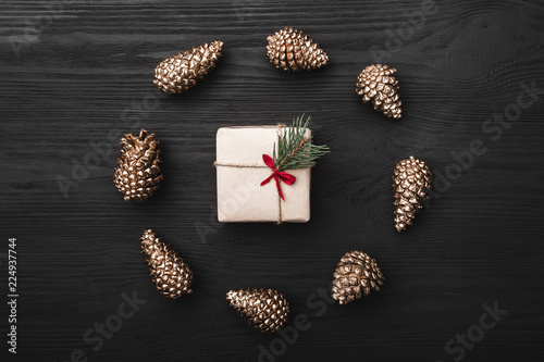 Upper, top view, of Christmas presents on a wooden black rustic background, suround by circle of golden pine cones