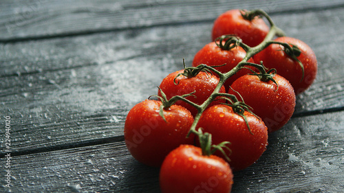Closeup branch with ripe cherry tomatoes on dark wooden table 