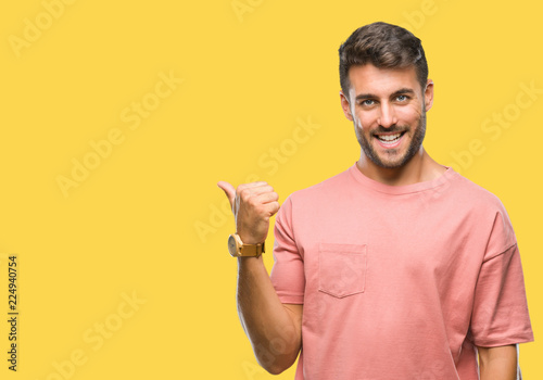 Young handsome man over isolated background smiling with happy face looking and pointing to the side with thumb up.