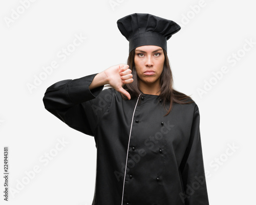 Young hispanic cook woman wearing chef uniform with angry face, negative sign showing dislike with thumbs down, rejection concept