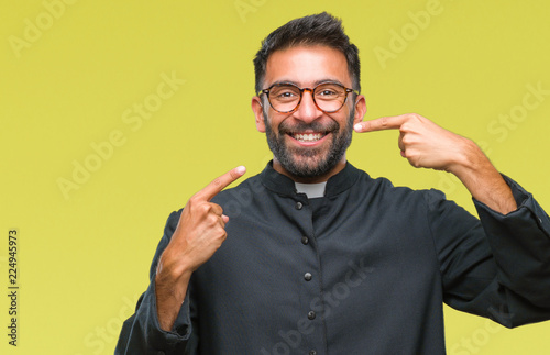 Adult hispanic catholic priest man over isolated background smiling confident showing and pointing with fingers teeth and mouth. Health concept.