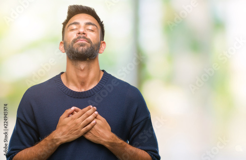 Adult hispanic man over isolated background smiling with hands on chest with closed eyes and grateful gesture on face. Health concept. photo
