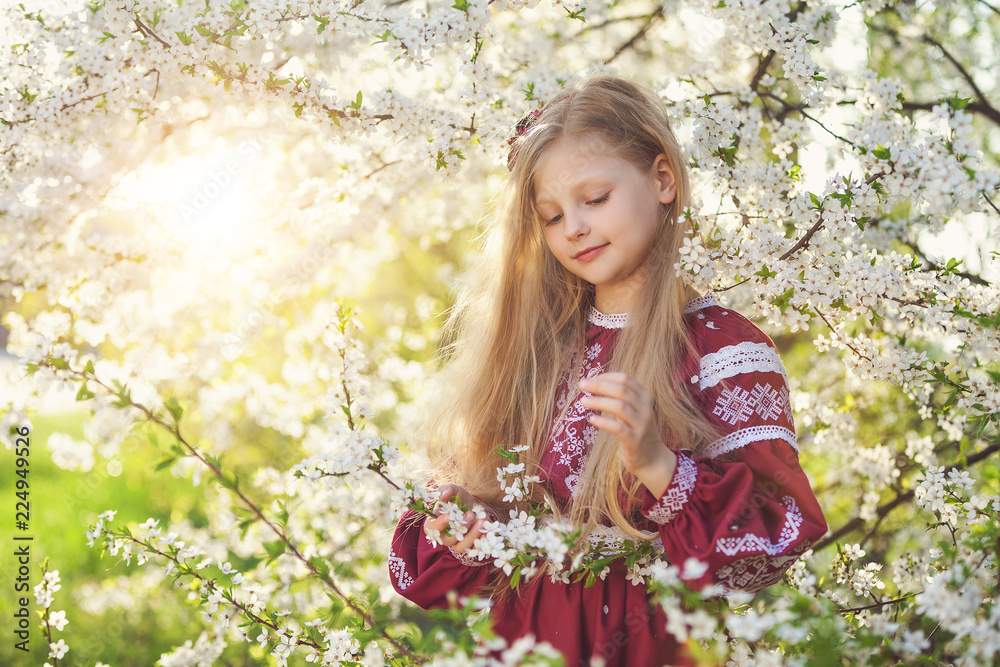 Lovely lttle girl stands under a blooming plum in park in ethnic ukrainian dress Lovely lttle girl stands under a blooming plum in park in ethnic ukrainian dress