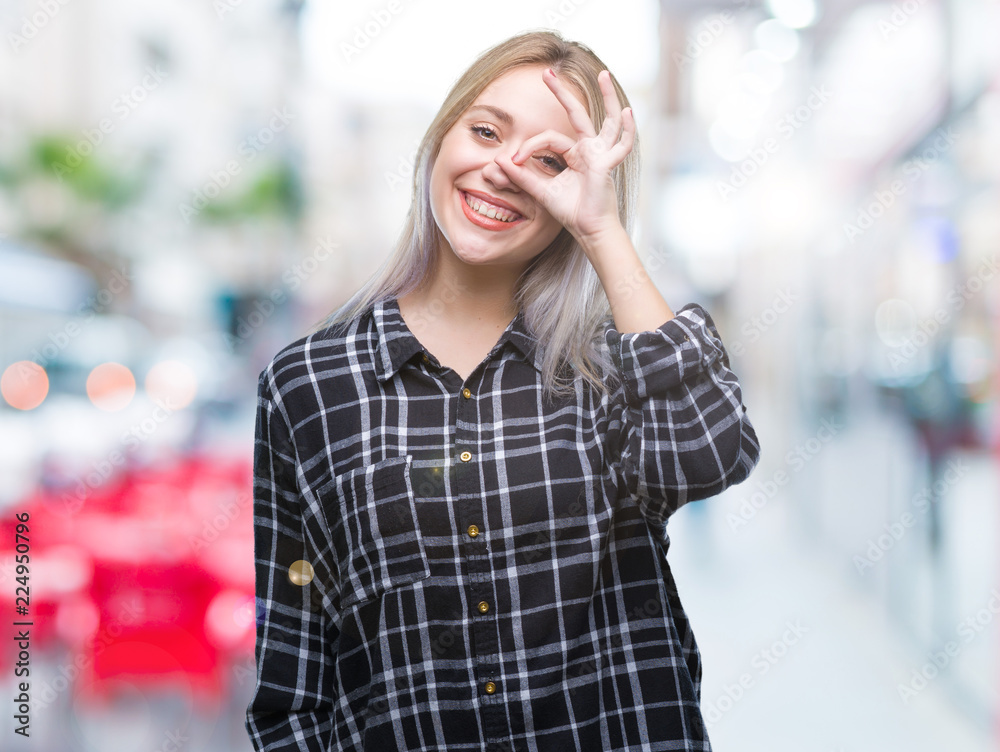 Fototapeta premium Young blonde woman over isolated background doing ok gesture with hand smiling, eye looking through fingers with happy face.