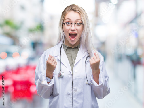 Young blonde doctor woman over isolated background celebrating surprised and amazed for success with arms raised and open eyes. Winner concept.