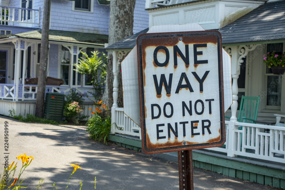 one way do not enter black & white sign with rusted edges on a summer suburban street in middle America homes with big white porches