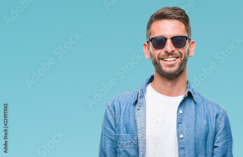 Young handsome man wearing sunglasses over isolated background looking away to side with smile on face, natural expression. Laughing confident.