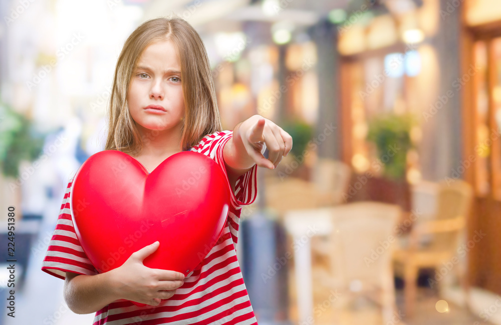 Young beautiful girl holding red heart over isolated background pointing with finger to the camera and to you, hand sign, positive and confident gesture from the front Young beautiful girl holding red heart over isolated background pointing with finger to the camera and to you, hand sign, positive and confident gesture from the front