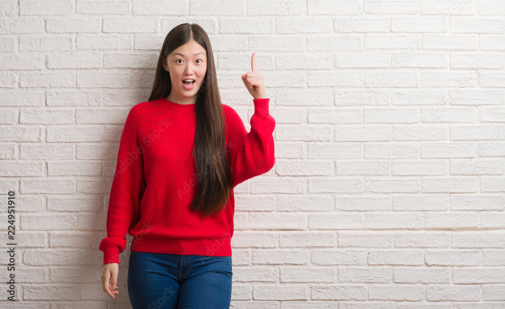 Young Chinese woman over brick wall pointing finger up with successful idea. Exited and happy. Number one. Young Chinese woman over brick wall pointing finger up with successful idea. Exited and happy. Number one.