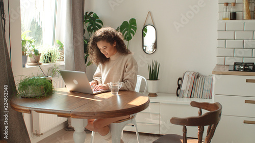 Charming young woman typing on laptop computer in a kitchen. photo