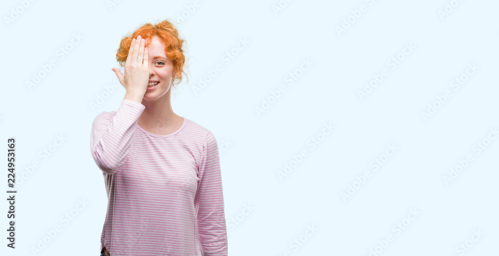 Young redhead woman covering one eye with hand with confident smile on face and surprise emotion. Young redhead woman covering one eye with hand with confident smile on face and surprise emotion.