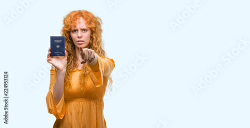 Young redhead woman holding passport of Germany pointing with finger to the camera and to you, hand sign, positive and confident gesture from the front