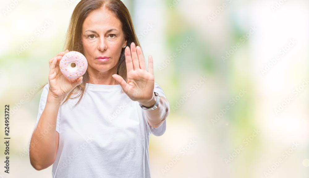 Middle age hispanic woman eating pink donut over isolated background with open hand doing stop sign with serious and confident expression, defense gesture Middle age hispanic woman eating pink donut over isolated background with open hand doing stop sign with serious and confident expression, defense gesture