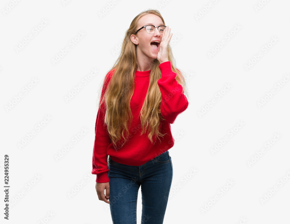 Blonde teenager woman wearing red sweater shouting and screaming loud to side with hand on mouth. Communication concept. Blonde teenager woman wearing red sweater shouting and screaming loud to side with hand on mouth. Communication concept.