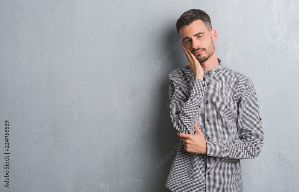 Young adult man standing over grey grunge wall thinking looking tired and bored with depression problems with crossed arms. Young adult man standing over grey grunge wall thinking looking tired and bored with depression problems with crossed arms.