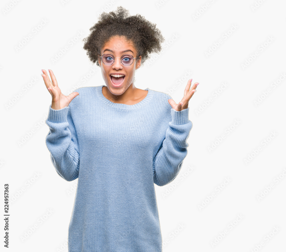 Young afro american woman wearing glasses over isolated background celebrating crazy and amazed for success with arms raised and open eyes screaming excited. Winner concept Young afro american woman wearing glasses over isolated background celebrating crazy and amazed for success with arms raised and open eyes screaming excited. Winner concept