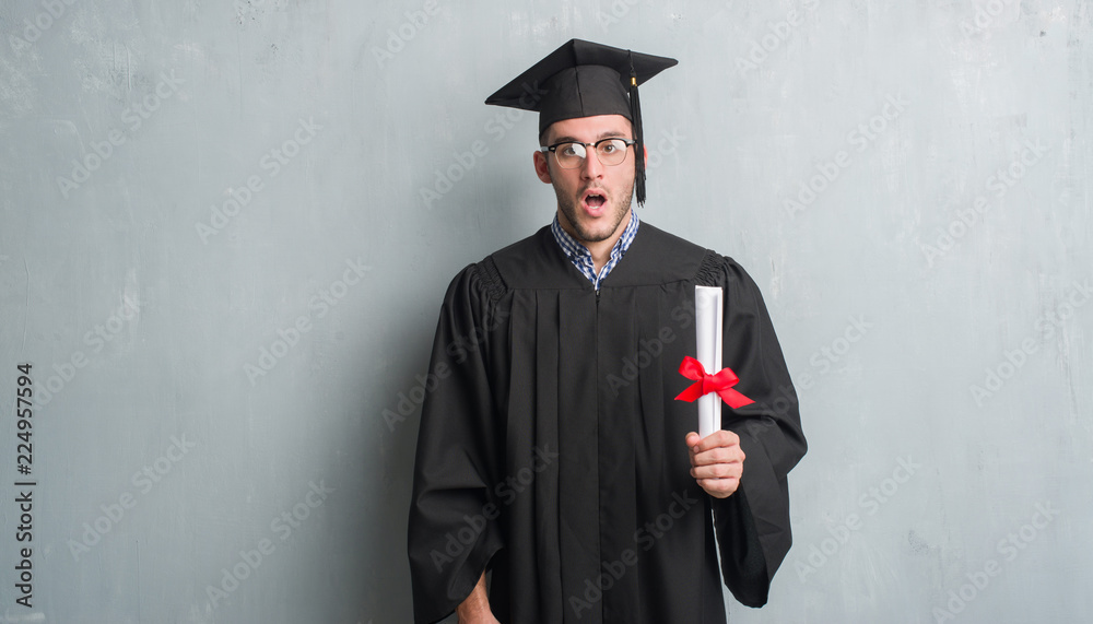 Young caucasian man over grey grunge wall wearing graduate uniform ...