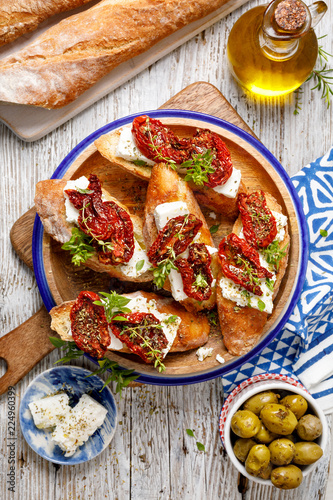 Bruschetta, toasted slices of bread with feta cheese, dried tomatoes, olive oil and fresh aromatic herbs, on a plate on a wooden table, top view. Delicious Mediterranean vegetarian   appetizer